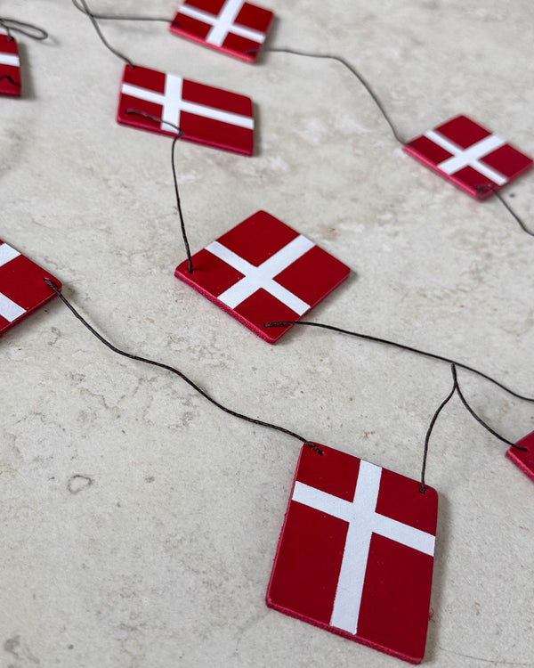 SALUT flaggspel med Dannebrog-flaggor i rött läder på svart snöre lagt på ljus stenyta