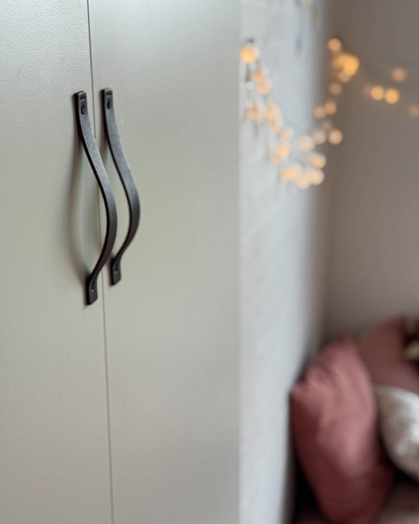 BAND handtag i mörkbrunt läder på ljus garderob med två dörrar, ljusslinga och rosa kuddar i bakgrunden