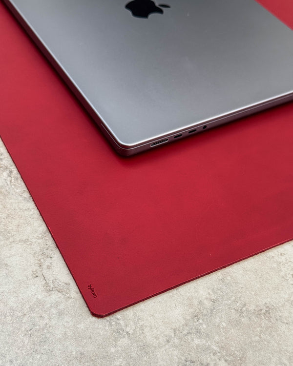 XXL DESK skrivunderlägg i rött läder med byRavn-prägling under laptop på ljus bordsskiva