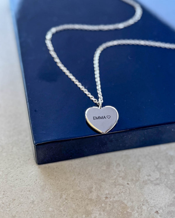 LUV QUOTE namnhalsband i silverfärgat rostfritt stål med "EMMA" ♡ graverat på hjärthänge, liggande på mörkblå presentask