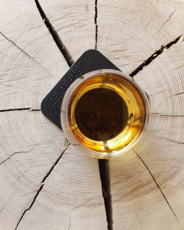 MOKKA fyrkantigt glasunderlägg i svart läder med gravyren "Ice ice baby" under whiskyglas på träskiva sett ovanifrån