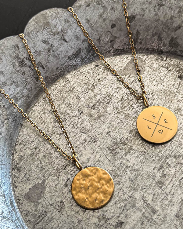 MOON X halsband i guldpläterat stål med kors och initialerna "S E L" och hjärta graverat, hamrat mynt bredvid, på zinkfat