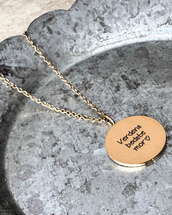 SIA QUOTE SCRIPT halsband i guldpläterat stål med handskriften "Verdens bedste mor" ♡ graverad, liggande på zinkfat