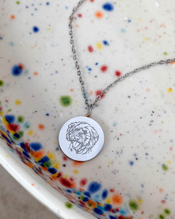 SIA PORTRAIT halsband i silverfärgat rostfritt stål med teckning av en lockig hund graverad på runt hänge, på prickigt fat