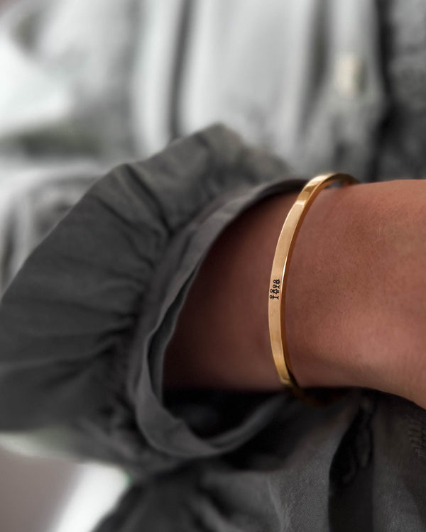 VENUS STICK armband i guldpläterat stål med graverad tändsticksfamilj, buret runt handleden till grå blus