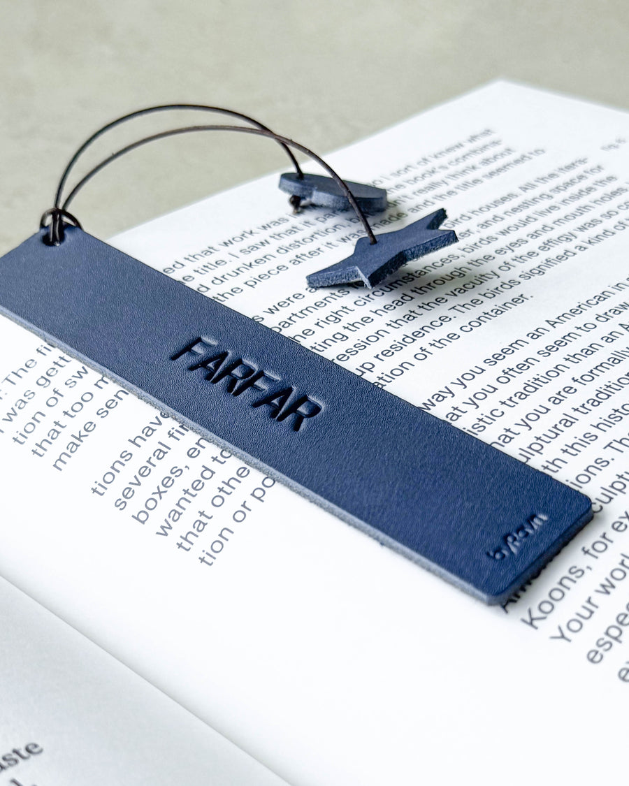 PAGE bokmärke i mörkblått läder med gravyren "Farfar" liggande på en uppslagen bok med stjärna och hjärta på snöre