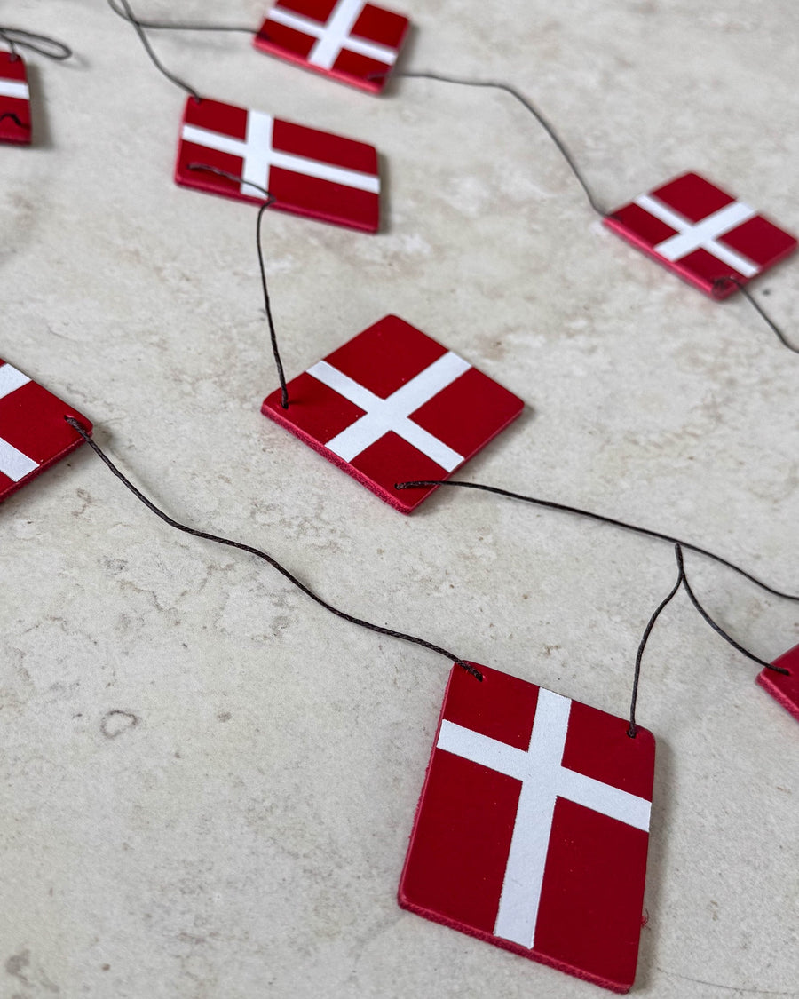 SALUT flaggspel med Dannebrog-flaggor i rött läder på svart snöre lagt på ljus stenyta