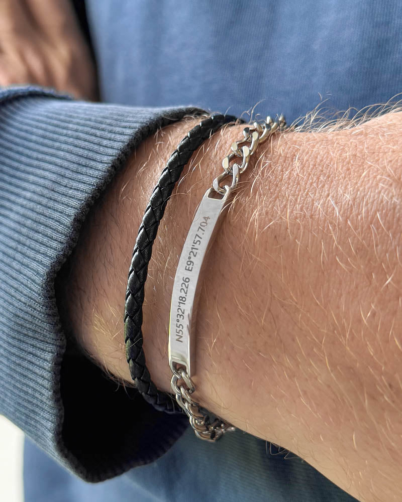 ARA armband i silverfärgat rostfritt stål med koordinaterna "N55°32'18.226 E9°21'57.704" graverade, buret med svart flätat läderarmband
