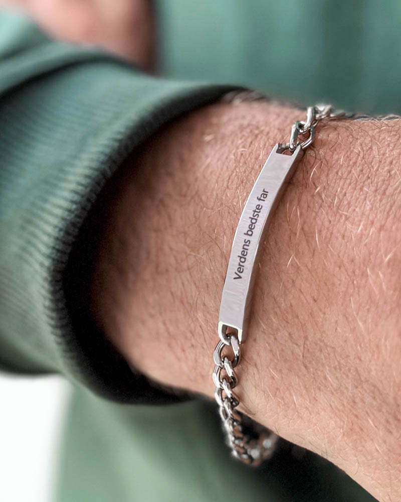 ARA armband i silverfärgat rostfritt stål med gravyren "Verdens bedste far" runt en mans handled, grön sweatshirt