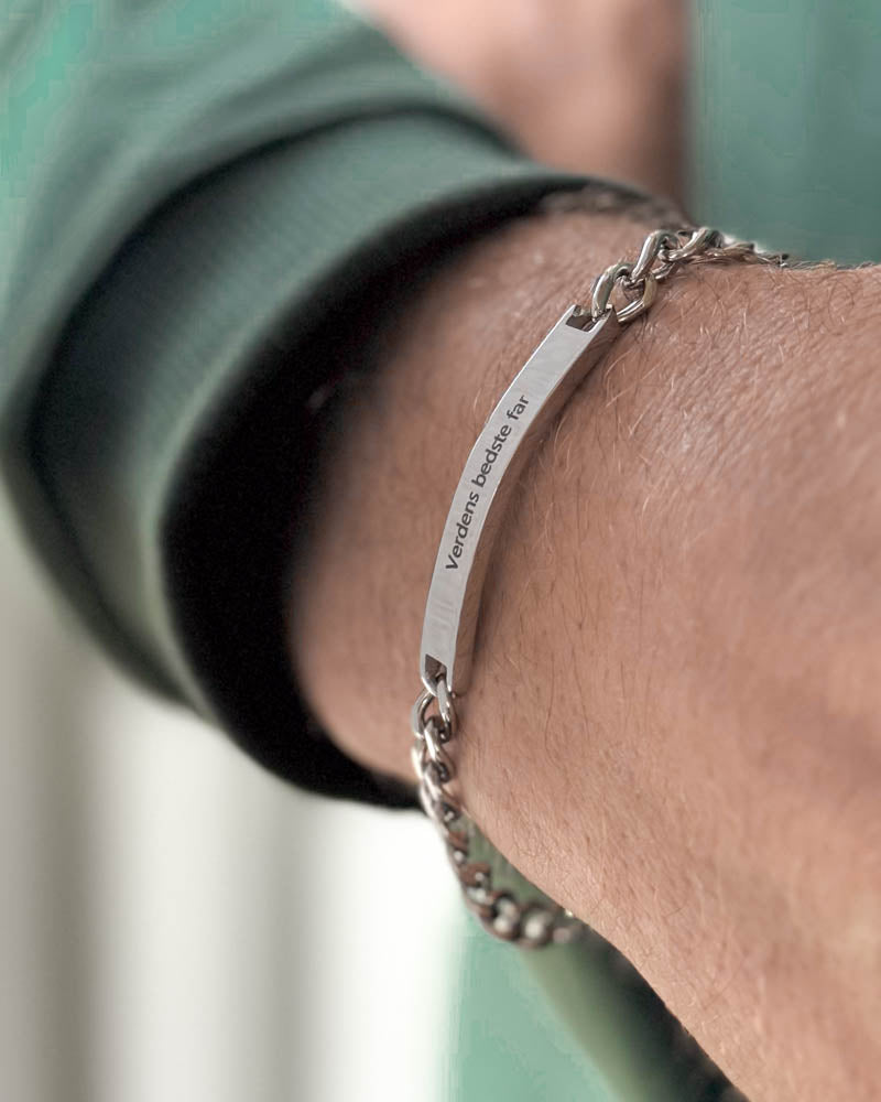 ARA armband i silverfärgat rostfritt stål med "Verdens bedste far" graverat på avlång bricka, sett snett från sidan runt handleden