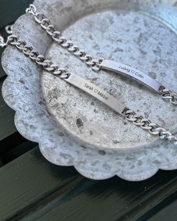 ARA armband i silverfärgat stål, matt bricka med "Sarah ♡ Mikkel" och blank bricka med "Ludvig ♡ Colin" graverat, på zinkfat