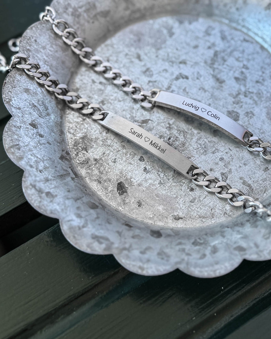 ARA armband i silverfärgat stål, matt bricka med "Sarah ♡ Mikkel" och blank bricka med "Ludvig ♡ Colin" graverat, på zinkfat