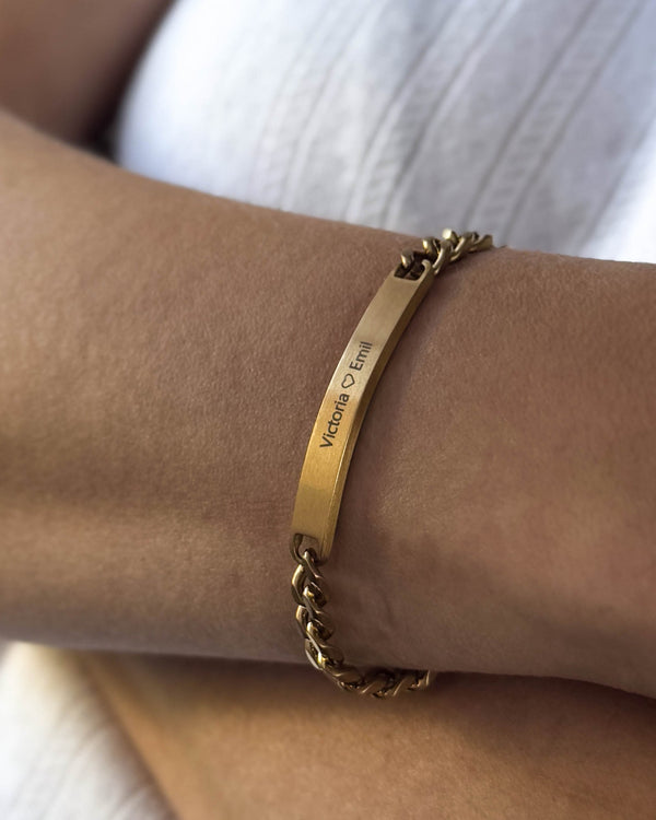 AVA armband i borstat guldpläterat stål med personlig gravyr "Victoria ♡ Emil" buret runt handleden