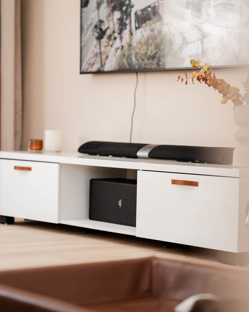 BAND handtag i cognac läder på vit tv-bänk med två lådor, soundbar och tv på väggen i vardagsrummet