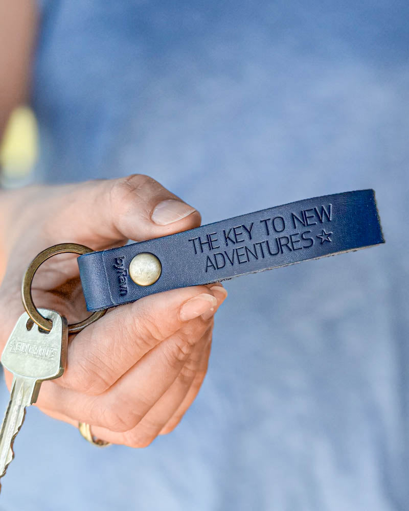 BOND nyckelring i mörkblått läder med personlig gravyr "The key to new adventures" ☆, hålls i handen med nyckel