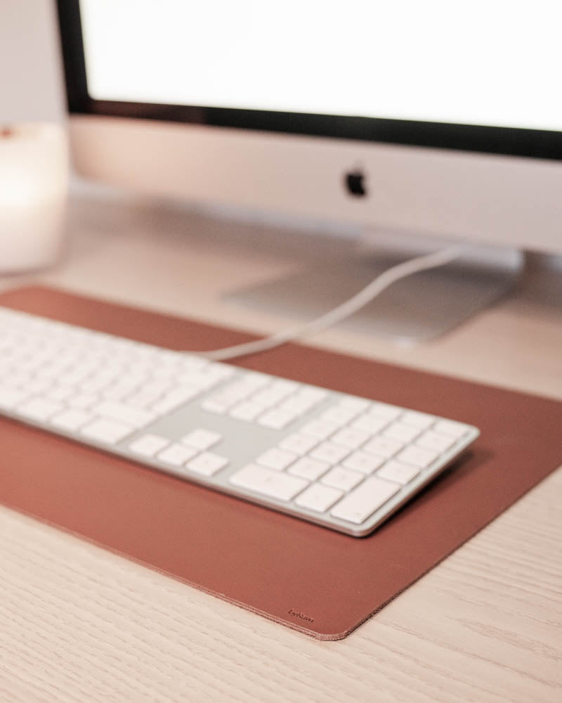 DESK skrivunderlägg i cognac läder under vitt tangentbord framför iMac på ljust träskrivbord