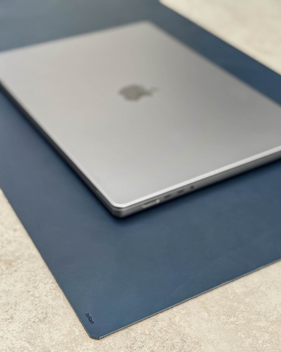 XXL DESK skrivunderlägg i mörkblått läder med byRavn-prägling under laptop på ljus bordsskiva