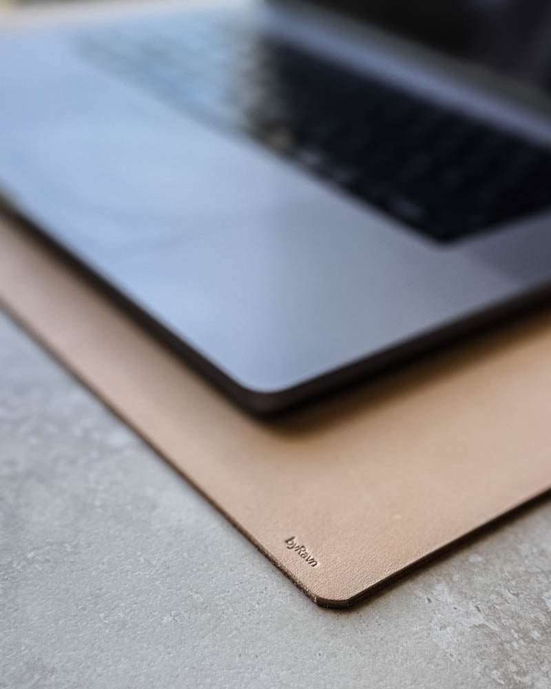 DESK skrivunderlägg i naturfärgat läder med byRavn-prägling under laptop på ljus bordsskiva