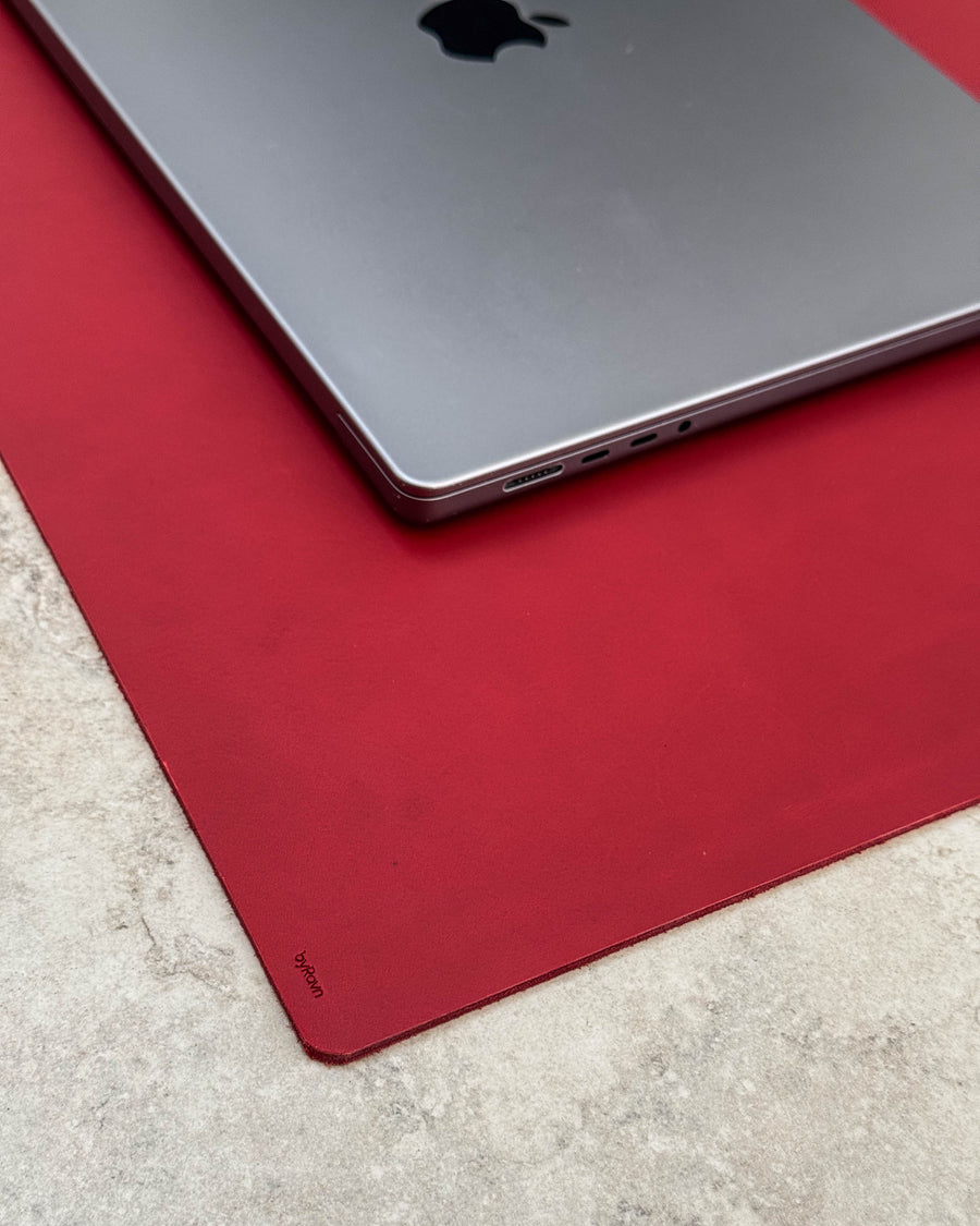 XXL DESK skrivunderlägg i rött läder med byRavn-prägling under laptop på ljus bordsskiva
