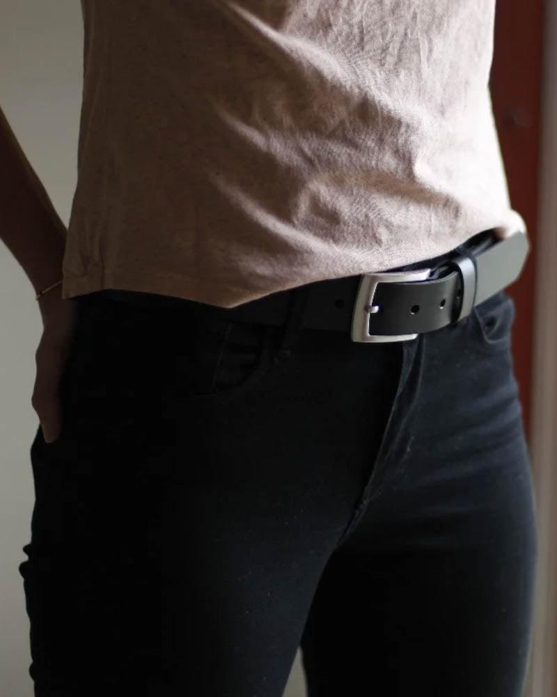 EDGE bälte i svart läder buret av kvinna i svarta byxor och beige t-shirt, sett från sidan