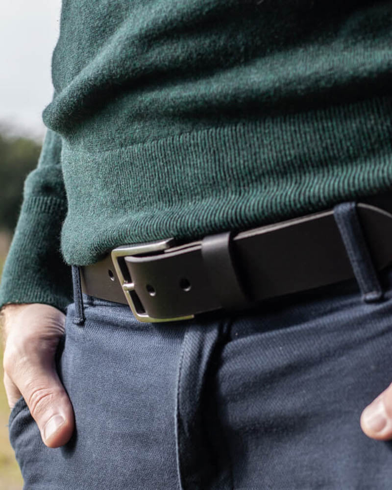 EDGE bälte i svart läder med stålspänne buret i blå byxor med mörkgrön stickad tröja utomhus