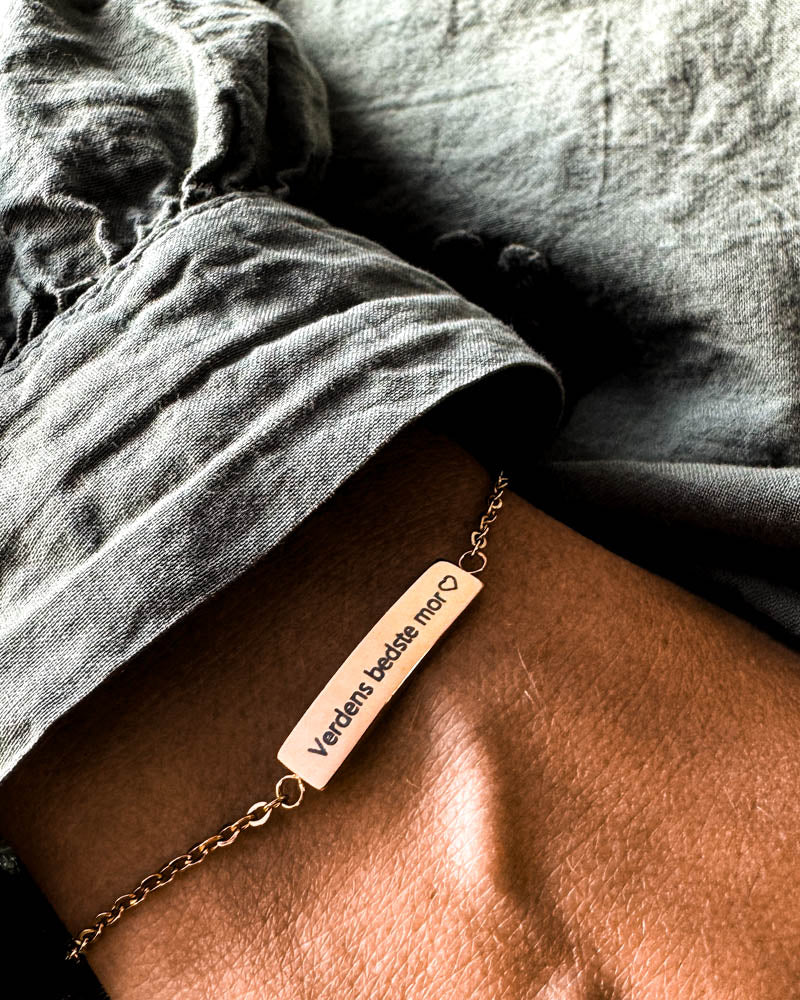 EVI armband i guldpläterat stål med gravyren "Verdens bedste mor" ♡ runt handleden, grå linneskjorta