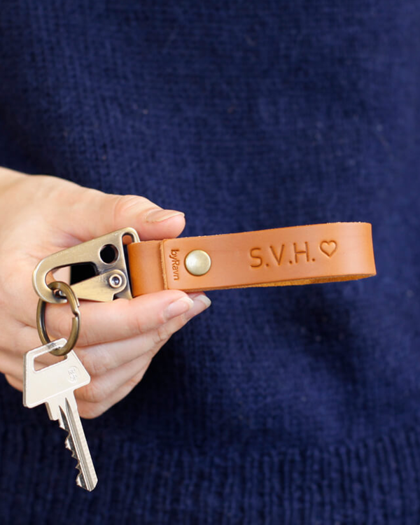 HOOK nyckelring i cognac läder som hålls i handen med nyckel och initialerna "S.V.H." ♡ graverade