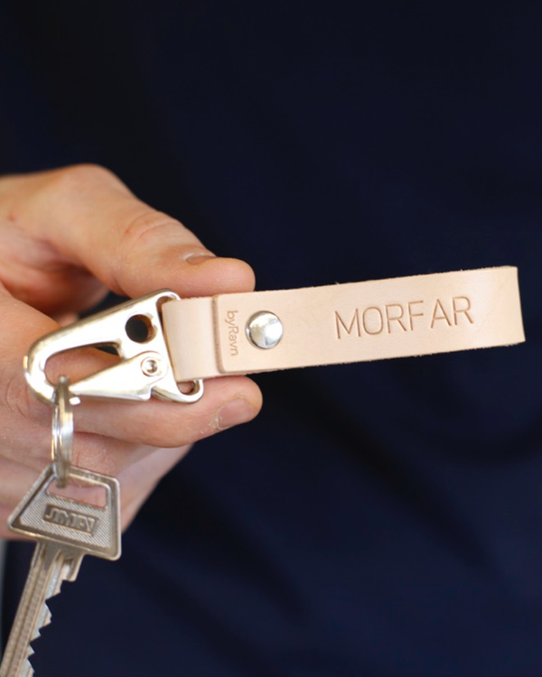 HOOK nyckelring i naturfärgat läder med karbinhake i stål och gravyren "Morfar", hålls i handen med nyckel