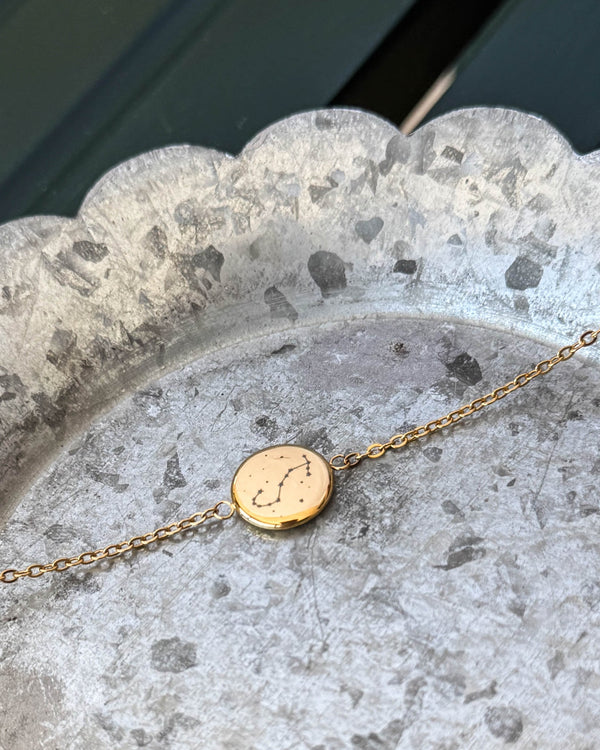 IBI STAR armband i guldpläterat stål med stjärnbilden Skorpionen graverad på rund bricka, liggande på zinkfat