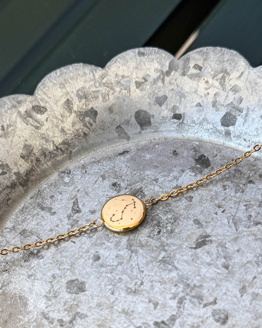 IBI STAR armband i guldpläterat stål med stjärnbilden Skorpionen graverad på rund bricka, liggande på zinkfat
