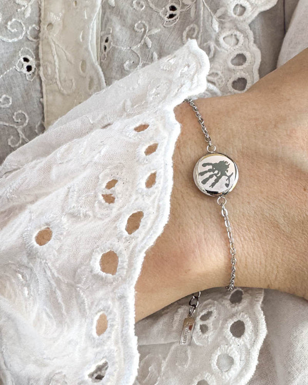 IBI MOTIF armband i silverfärgat rostfritt stål med graverat handavtryck, buret runt handleden till vit spetsblus