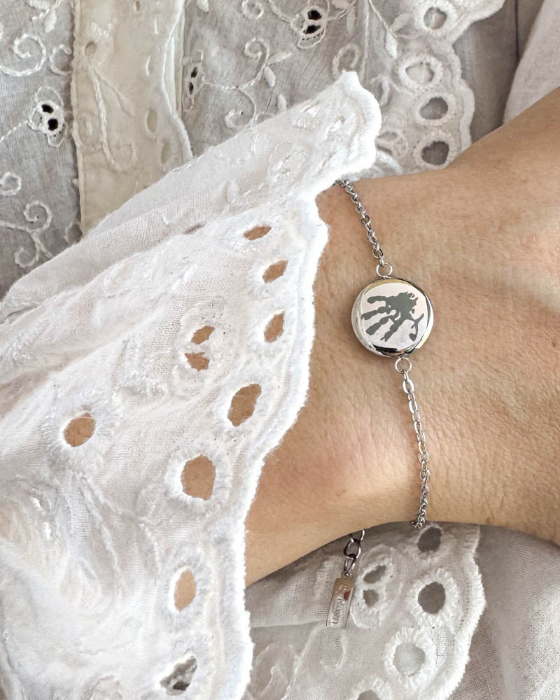 IBI MOTIF armband i silverfärgat rostfritt stål med graverat handavtryck, buret runt handleden till vit spetsblus