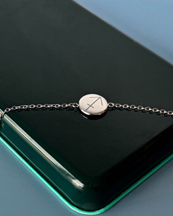 IBI STAR armband i silverfärgat rostfritt stål med stjärntecknet Skytten graverat på rund bricka, liggande på mörkgrön ask