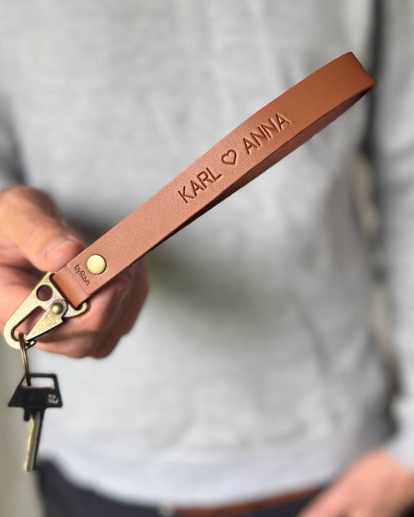 IRON nyckelring i cognac läder med namnen "Karl ♡ Anna" graverade, hålls i handen med nyckel