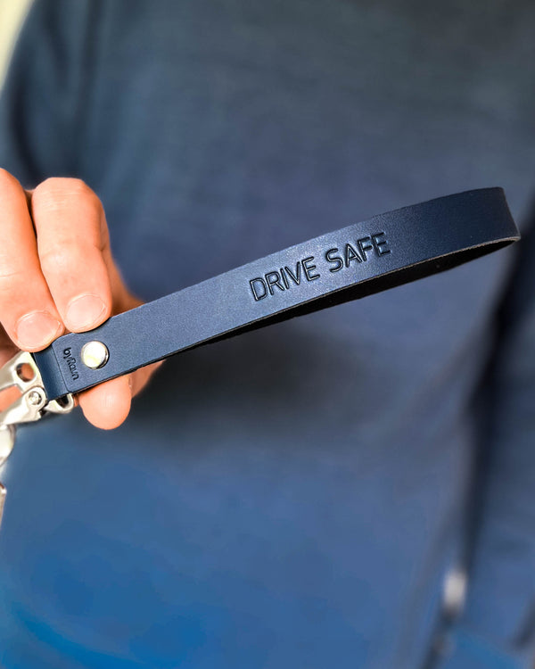 IRON nyckelring i mörkblått läder med lång stropp och gravyren "Drive safe", hålls i handen