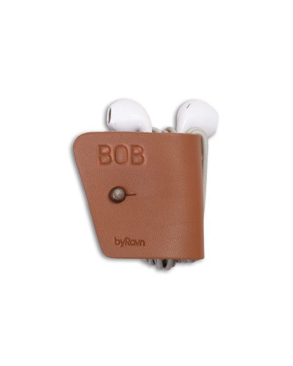 KAX hörlurshållare från byRavn i cognac läder med gevärsknapp i antik mässing och namnet "Bob" graverat, med earpods