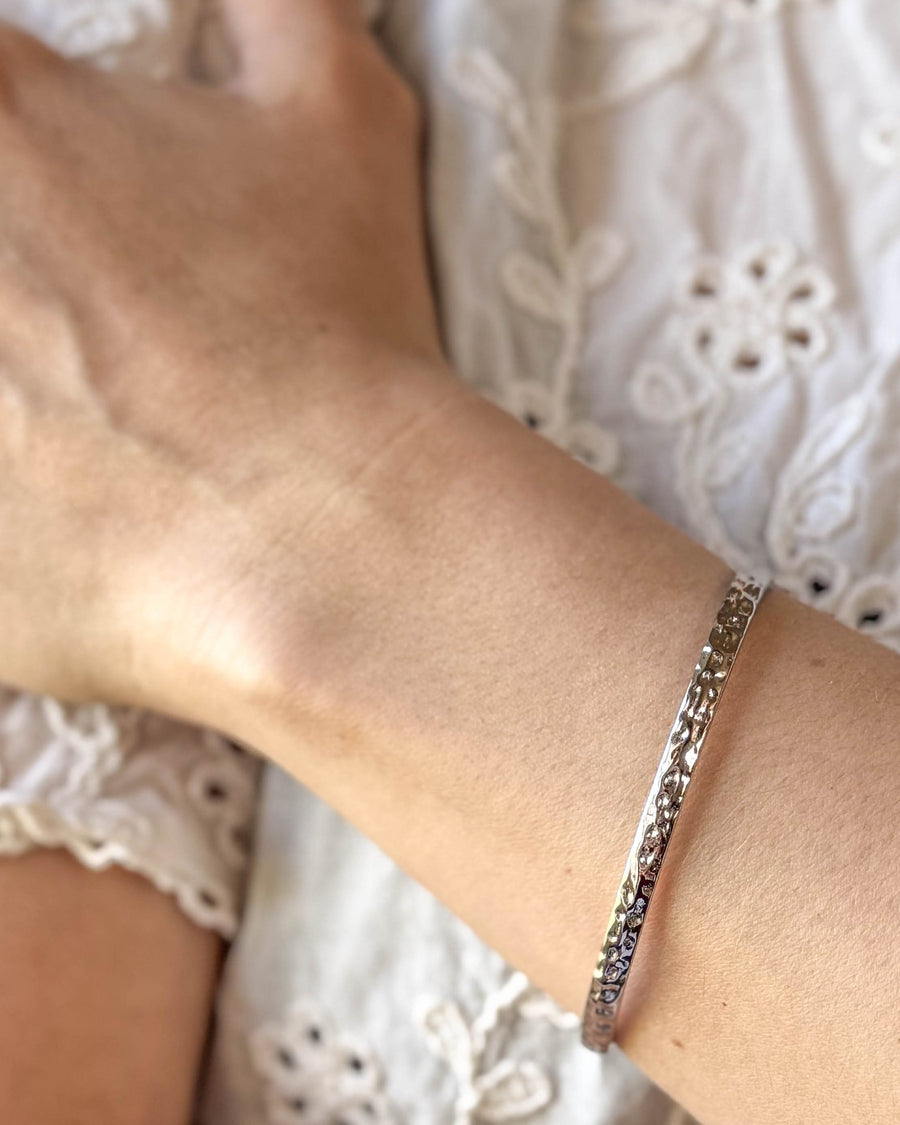 LUNA armband i silverfärgat rostfritt stål, hamrad armring buren runt handleden till vit spetsblus