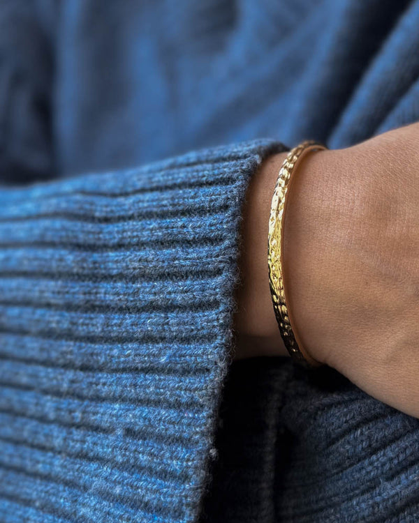 LUNA armband i guldpläterat stål, hamrad armring buren runt handleden till blå stickat