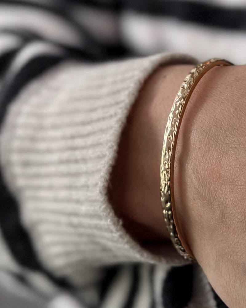 LUNA armband i guldpläterat stål med hamrad yta runt handleden, vit stickat och randig blus