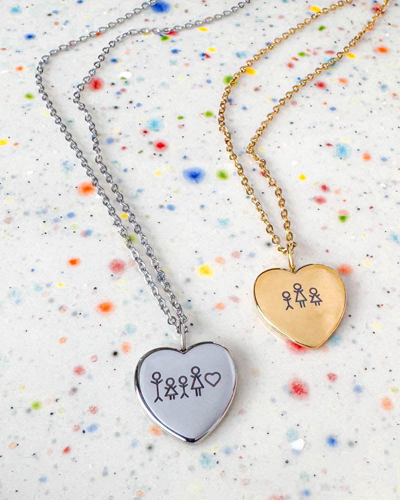 LUV STICK halsband i silverfärgat stål med tändsticksfamilj och hjärta graverat, bredvid guldpläterad variant med två figurer