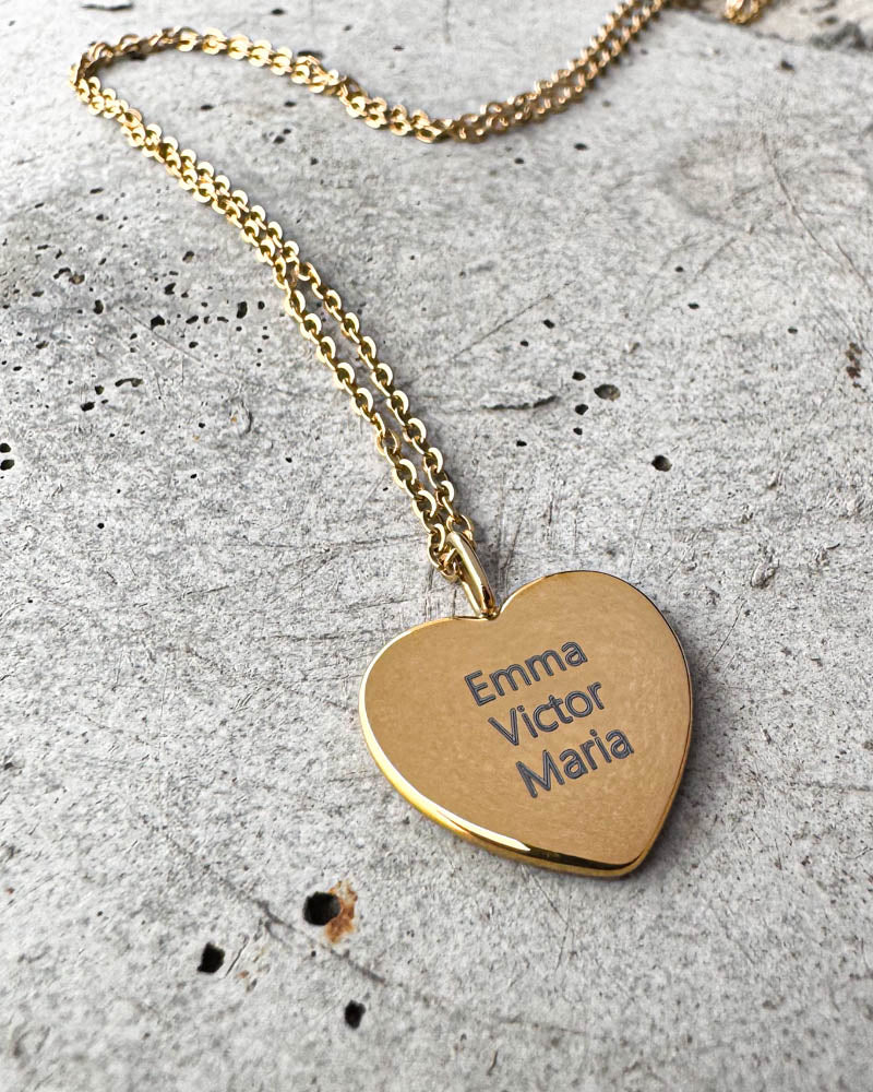 LUV QUOTE namnhalsband i guldpläterat stål med namnen "Emma Victor Maria" graverade på hjärthänge, liggande på betong