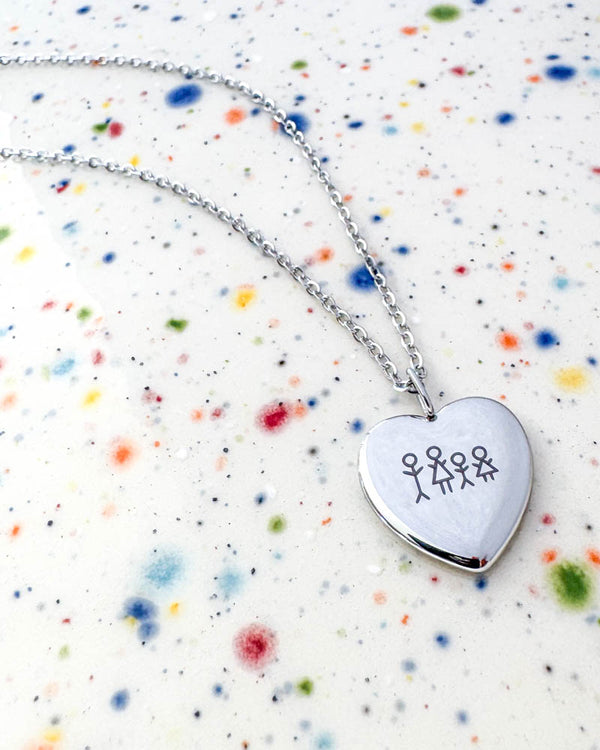 LUV STICK halsband i silverfärgat rostfritt stål med tändsticksfamilj på fyra graverad i hjärthänge, på prickig keramik