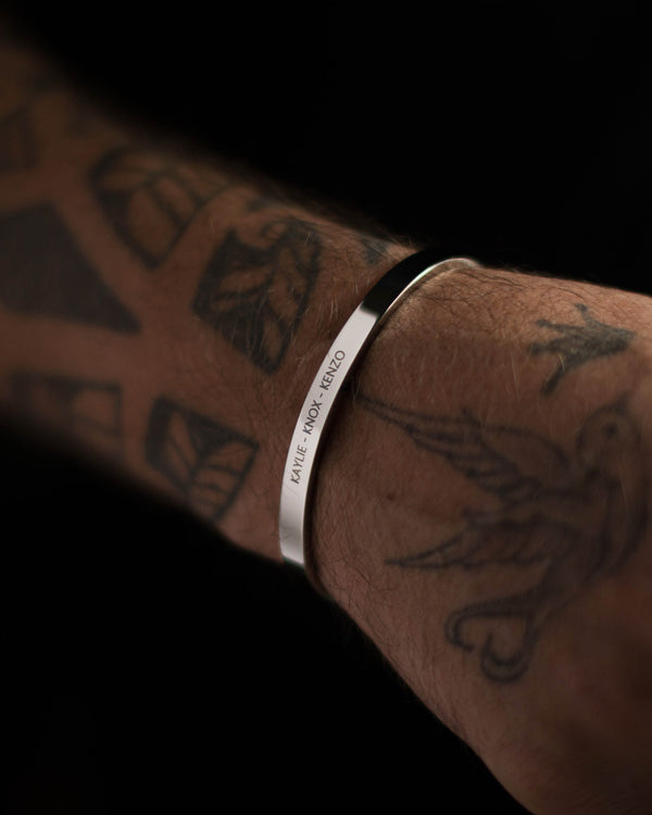 MARS armband i silverfärgat rostfritt stål med gravyren "Kaylie – Knox – Kenzo" på tatuerad mansarm