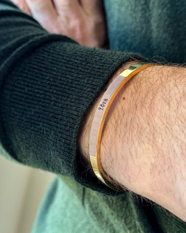 MARS STICK armband i guldpläterat stål med graverad tändsticksfamilj, buret runt handleden till mörkgrön stickat
