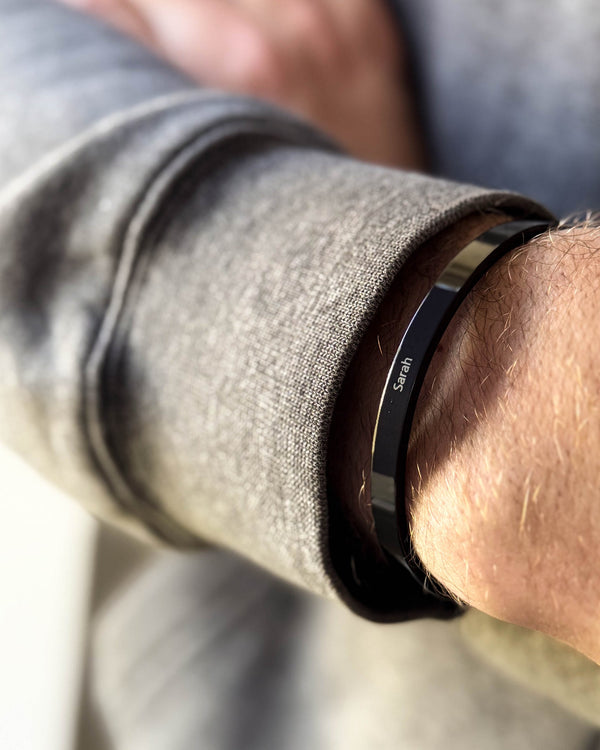 MARS armband i svart stål med namnet "Sarah" graverat, runt en mans handled, grå sweatshirt