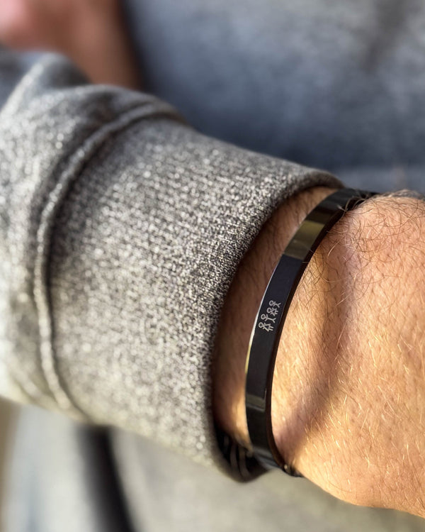MARS STICK armband i svart stål med graverad tändsticksfamilj, buret runt handleden till grå stickat