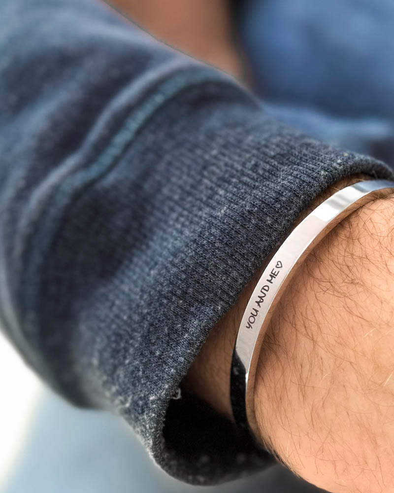 MARS SCRIPT armband i silverfärgat rostfritt stål med "You and me" ♡ graverat i handstil runt handleden, blå sweatshirt