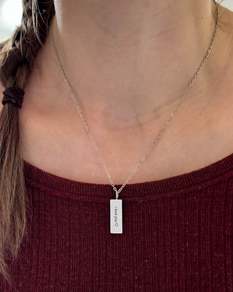 MIO halsband i silverfärgat rostfritt stål med gravyren "I love you" ♡ på rektangulärt hänge, buret runt halsen över vinröd topp