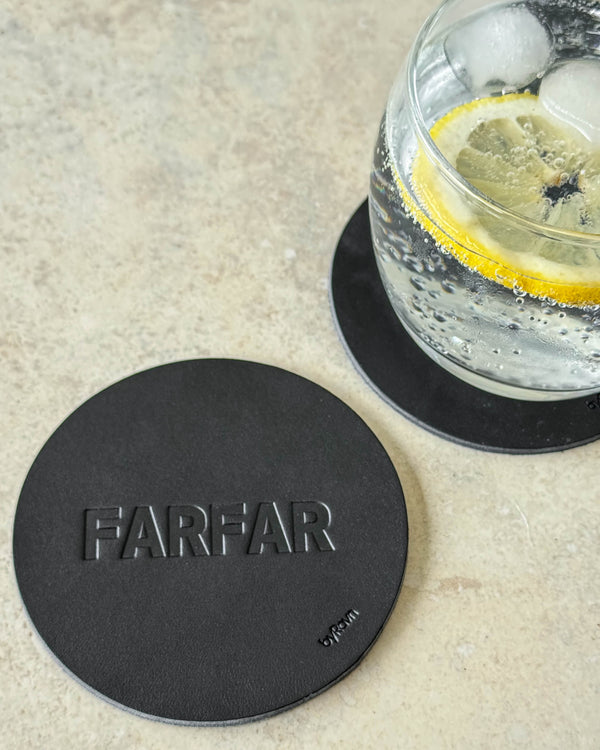 MOKKA glasunderlägg i svart läder präglat "Farfar" på ljust bord vid glas med gin och tonic och citronskiva