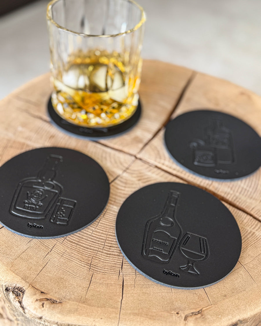 MOKKA sprit-glasunderlägg i svart läder präglade med rom, cognac och gin på träskiva vid kristallglas med whisky